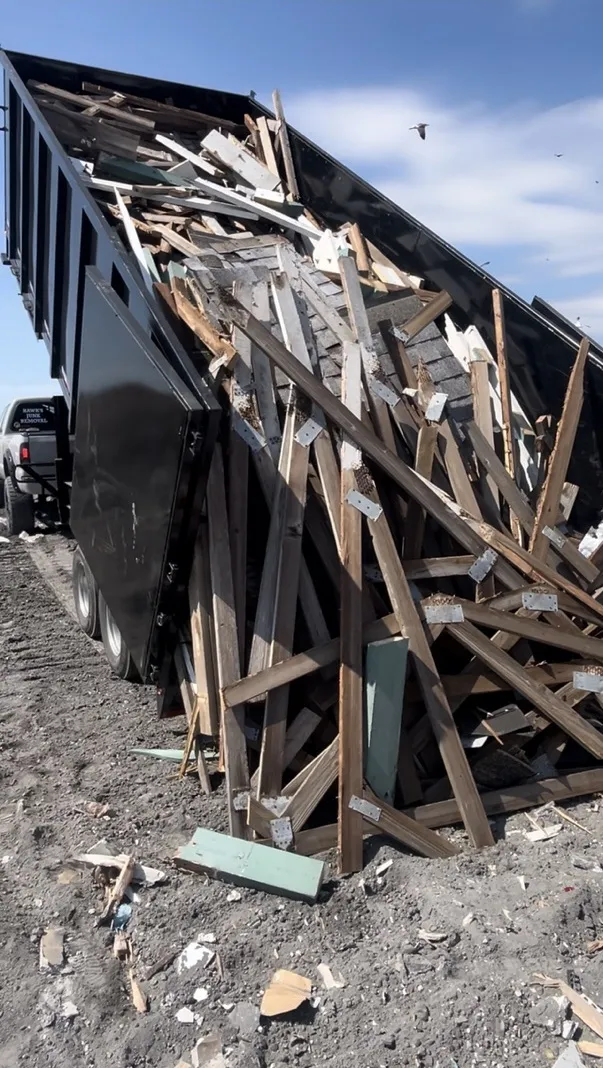 Dump trailer offloading a full load of demolished lumber and framing debris